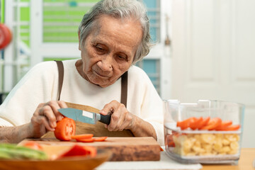 Elderly woman are cooking in their home kitchen and looking at digital tablets to learn how to cook, Slicing tomatoes to prepare for a salad.