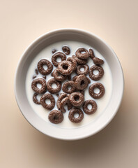 Top-down view of a white ceramic bowl with a small portion of dark chocolate cereal rings (Oreo-style texture), mostly submerged in fresh milk. Generous milk quantity, minimal cereal floating on top. 