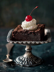 A refined studio food photography shot featuring a decadent chocolate brownie elegantly placed in a silver dessert dish. The brownie is styled with a dollop of whipped cream and topped with a glossy r