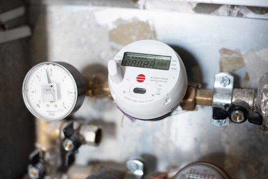 Close-up of a modern digital water meter with pressure gauge installed on a household pipe system. Concept of utility measurement, energy efficiency, infrastructure and resource control.