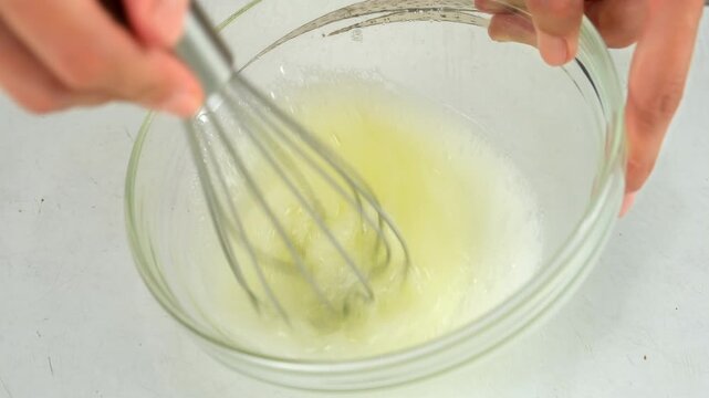 Woman hands cooking mixing sugar with egg white in glass bowl using metal whisk on kitchen at home. Recipe cuisine culinary ingredient. Baking, preparing food dish. Healthy protein in chicken eggs.