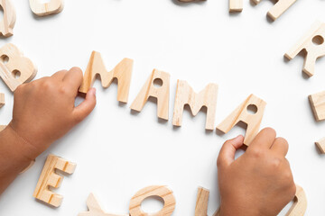 Child hands arranging wooden letters to spell MAMA on white background