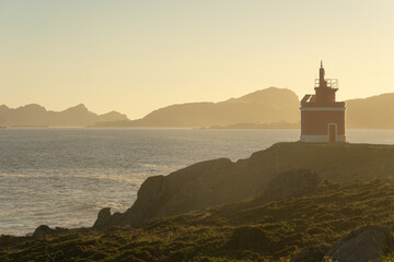 Punta Robaleira red lighthouse in Home cape at sunset in Rias Baixas zone in Galicia coast with Cíes islands in the background.