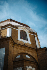 A low-angle view captures the rich architectural details of a historic building in Florence, Italy, showcasing its ornate window, textured brickwork, and tiled dome against a vivid blue sky.