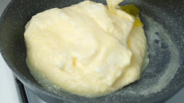 Woman putting omelet whipped mass in frying pan using spatula cooking on kitchen. Recipe cuisine culinary ingredient. Baking preparing food dish. Prepare super fluffy souffle egg omelet close-up.