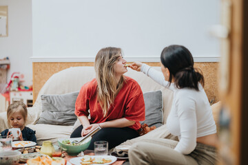 A warm gathering of two friends sharing food while a little girl plays nearby. This image captures friendship, care, and familial interaction in a cozy and casual environment.