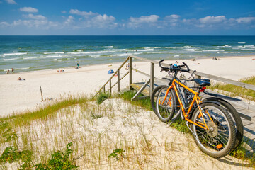 Two bicycles parked on a wooden ramp leading down to a wide, sunny beach of the Curonian spit, summer travel and active vacation