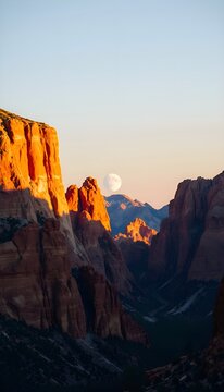 Moon over canyon at sunset. Scenic canyon landscape with red cliffs illuminated by sunset light and the moon rising above the mountains.