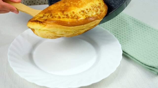 Putting fried omelet to plate from frying pan with wooden spatula cooking on kitchen. Recipe cuisine culinary ingredient. Preparing chicken eggs food dish. Super fluffy egg omelet close-up.