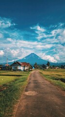 Fototapeta premium Mountain view with houses, road, and fields under a cloudy, blue sky