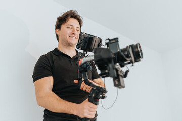 A young man skillfully handling a camera with a stabilizer in a bright room. Capturing moments and technically adjusting the device, he exemplifies focus and attentiveness during creative work.
