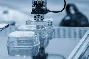 Close up scene material handling process the food container by robotic system from injection machine in the light blue scene.