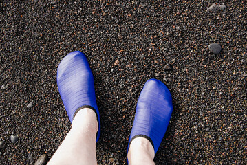 Woman's feet in underwater shoes on a black beach.
