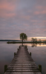 Obraz premium A tranquil twilight capture of a wooden pier on a serene, reflective lake.