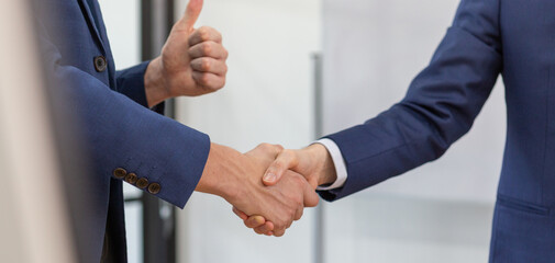 Close-up of two businessmen shaking hands with thumbs up gesture, symbolizing successful agreement, partnership, mutual trust, business deal, and positive collaboration in corporate setting.
