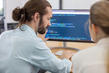 Software developer explaining code on computer screen to colleague in modern office, representing teamwork, programming, collaboration, software development, and tech industry environment.
