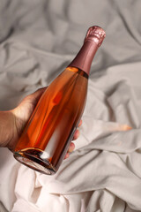 Wine bottle mockup with elegant champagne sparkling wine rose-colored liquid, held against soft white fabric, showcasing luxurious design and inviting ambiance for creative projects