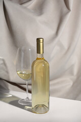 White Wine bottle mockup with glass of white wine on a minimalist table, featuring soft fabric backdrop, showcasing elegant design and inviting atmosphere for branding concepts