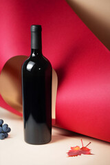 Wine bottle mockup displayed against vibrant red and beige backdrop, surrounded by grapes and autumn leaves, showcasing elegant design and creative concept for branding