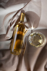 White wine bottle mockup with glass on elegant satin fabric, showcasing luxurious textures and soft lighting for sophisticated branding and design concepts