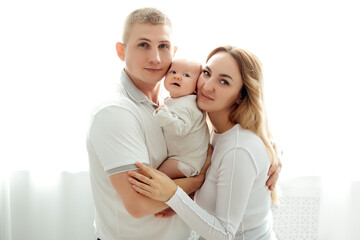 Fototapeta premium a young family mom and dad holding a newborn baby, hugging and kissing, a happy family with a small child on a white background