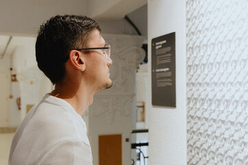 A young man looks at a painting in a room.