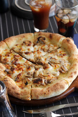 Freshly baked mushroom cheese pizza on wooden tray served with iced coffee and cola in glasses on dining table.