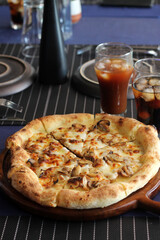 Freshly baked mushroom cheese pizza on wooden tray served with iced coffee and cola in glasses on dining table.