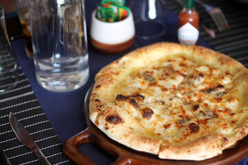 Freshly baked mushroom cheese pizza on wooden tray served with iced coffee and cola in glasses on dining table.