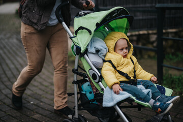 Obraz premium A young child in a yellow jacket sits in a bright green stroller while outdoors. They appear engaged in the scenery as a parent pushes the stroller along a paved pathway.