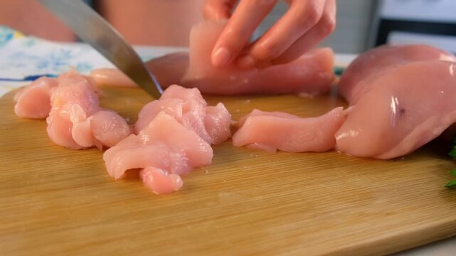 Chef woman hands cutting chicken breast into pieces on wooden board on kitchen. Culinary skills techniques, homemade preparing healthy meal, cook domestic food dish cuisine, fresh ingredients.