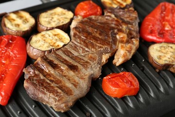 Electric grill with beef steaks and vegetables on grey table, closeup