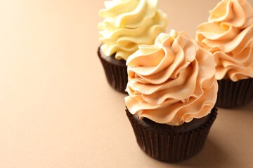 Delicious cupcakes with colorful cream on beige background, closeup. Space for text