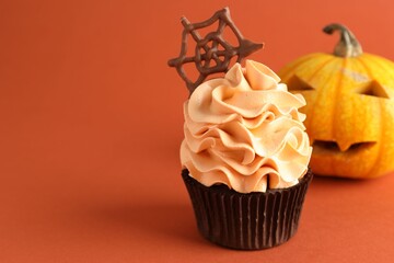 Delicious cupcake with chocolate web and pumpkin on coral background, closeup with space for text. Halloween celebration
