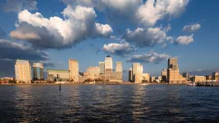 Docklands, London. A striking view of the Canary Wharf skyline at golden hour, with the setting sun illuminating the buildings and casting a warm glow across the water of the River Thames.