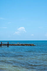 Obraz premium Wooden pier with stone breakwater in blue ocean under clear sky