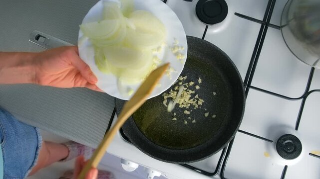 Woman cooking adding sliced onions into frying pan with hot oil on kitchen. Culinary skills techniques, homemade preparing healthy meal, cook domestic food dish cuisine, fresh ingredients.