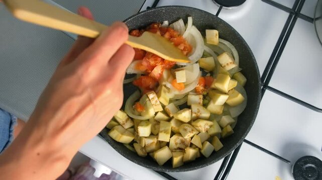 Chef woman hands cooking stirring onions eggplant tomatoes mixing in frying pan on gas stove on kitchen. Culinary techniques, homemade preparing healthy meal cook food dish, cuisine, seasoning garlic.