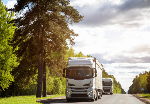A column of trucks with semi-trailers transports cargo along a country road. Logistics company for the delivery of consolidated cargo. GPS tracking and cargo insurance. Summer nature and forest. 