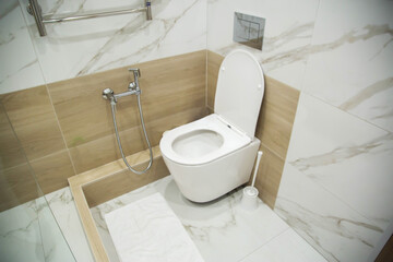 Modern wall-hung toilet against the background of a hygienic shower and porcelain tiles on the...