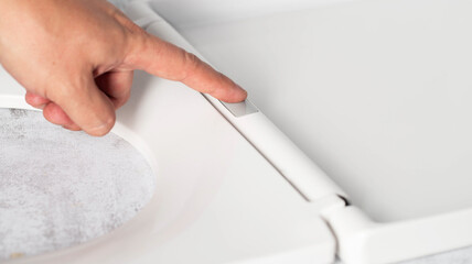 Close-up of finger pressing button on modern toilet seat cover to remove and disengage, close-up