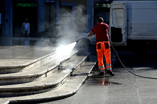 street cleaning in old European city. high pressure water jet washing of exterior stone stair by rubber hose. elevation and pavement washing concept. worker in red and orange work cloths. rubber boots