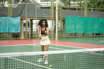 Confident African tennis player in sportswear concentrating before her serve, demonstrating focus and athletic form