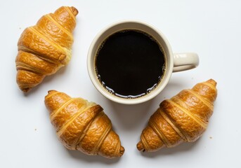 Overhead shot of coffee in a mug with croissants on a white surface.