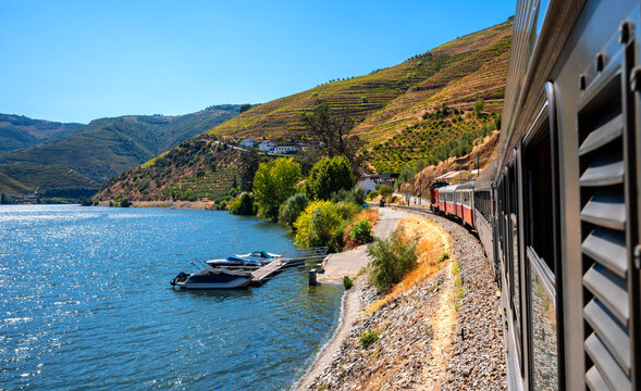 Panorama of the Douro Valley in northern Portugal photographed from the train. Picturesque vineyards, boats and houses at Portugal's most beautiful railway line along the riverbank on a summer day.