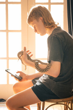 Teenage boy holding pet snake taking selfie with mobile phone