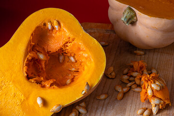 Detailed close-up of a halved butternut squash with seeds and pulp visible, placed on a wooden cutting board. Some loose seeds and fibrous pulp are scattered around, highlighting natural textures