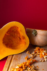 Fresh halved butternut squash displayed on a wooden cutting board with seeds and pulp scattered around, set against a bold red background