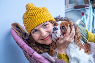 Woman in cozy yellow hat enjoys autumn afternoon on balcony with dog, wrapped in blanket, embracing companionship during menopause, showcasing warmth and comfort