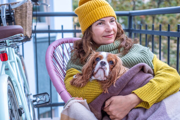 Woman enjoying autumn on a balcony, wrapped in a blanket with her dog, embracing warmth and companionship during midlife and menopause, creating a cozy atmosphere
